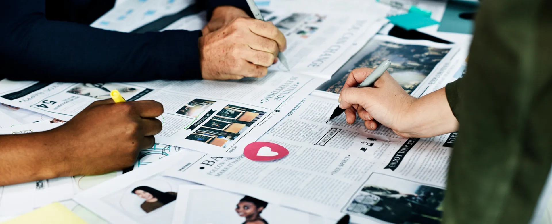 Hands reviewing printed newspaper pages on a desk