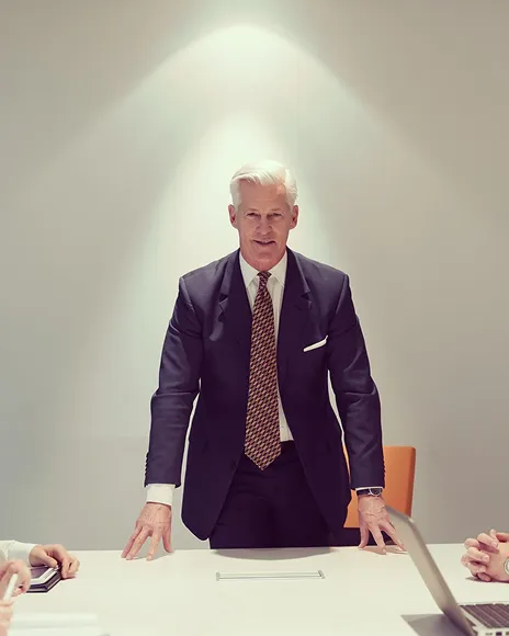 Senior founder standing at a boardroom table, representing founder authority positioning