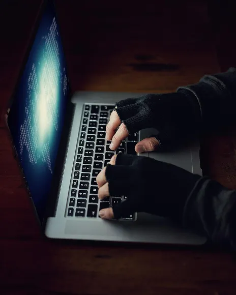 Hooded person typing on a laptop in the dark, representing anonymous burner accounts