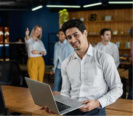 Smiling founder holding a laptop in a busy office